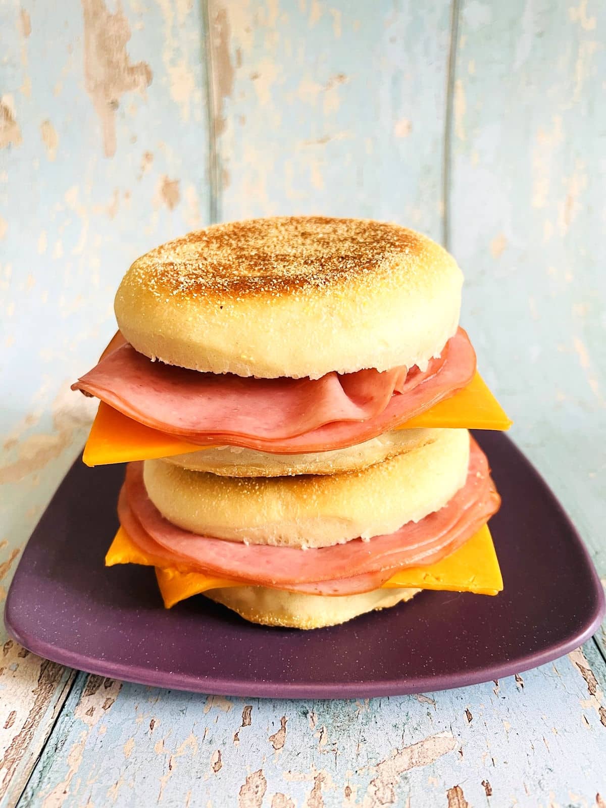 English muffin sandwiches with ham and cheese, stacked on purple plate.