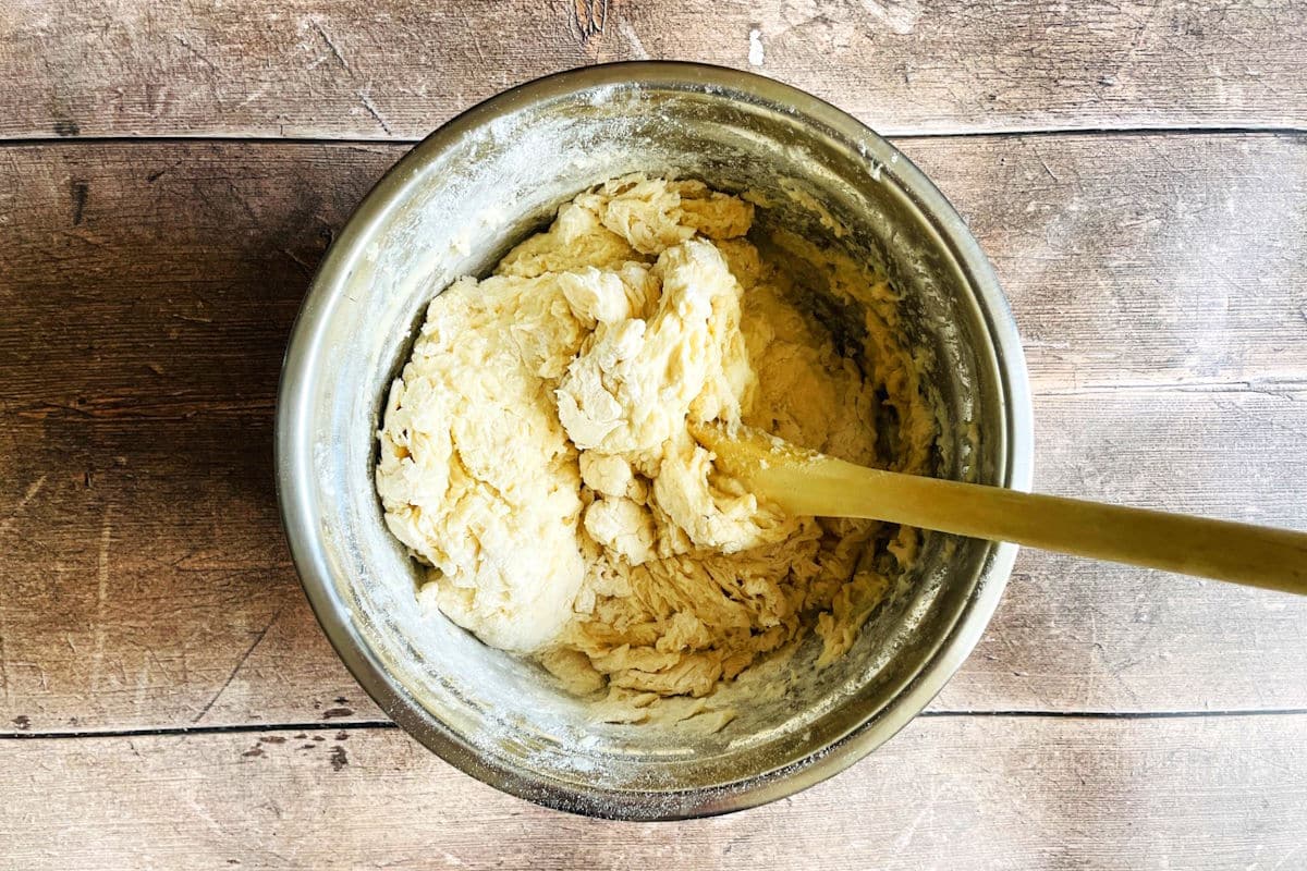 English muffin dough in bowl with wooden spoon.