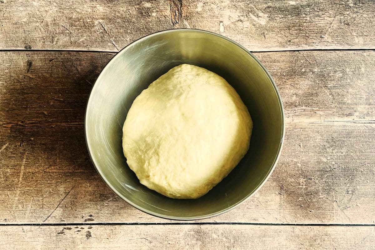 English muffin dough ball in buttered bowl.