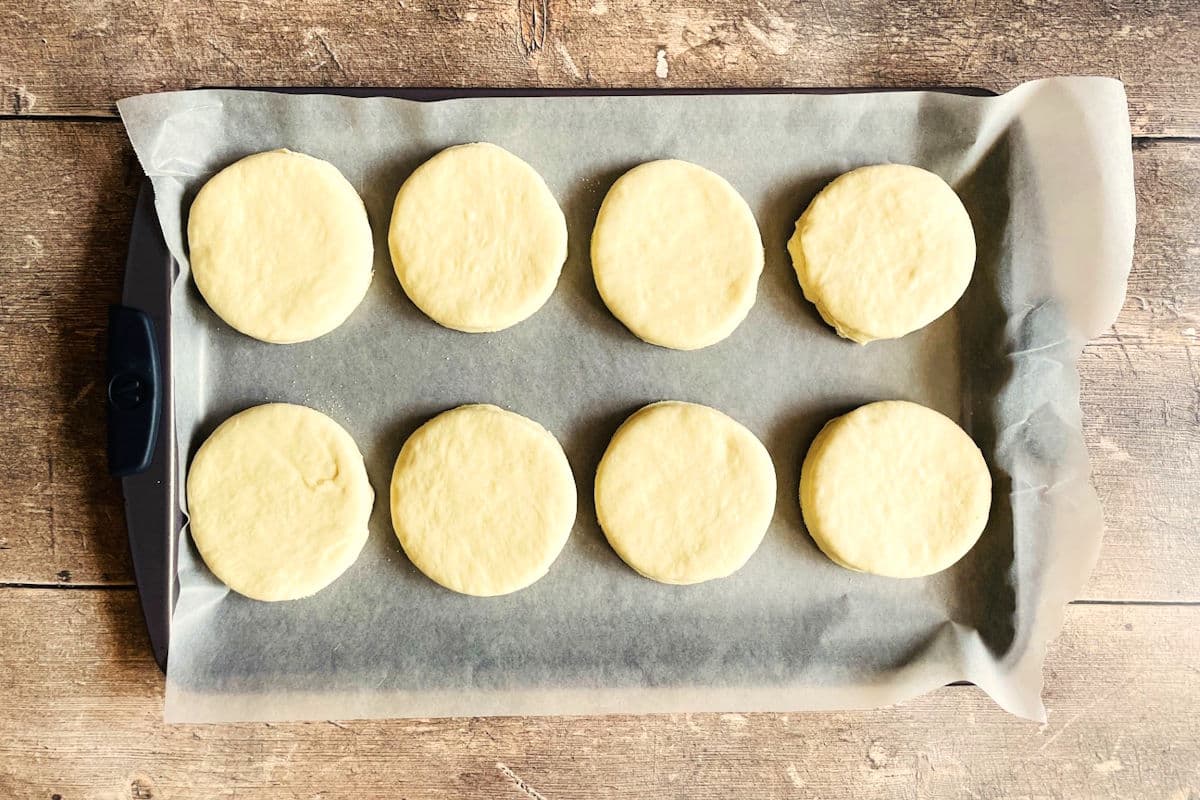 English muffin dough rounds on wax paper lined sheet pan.