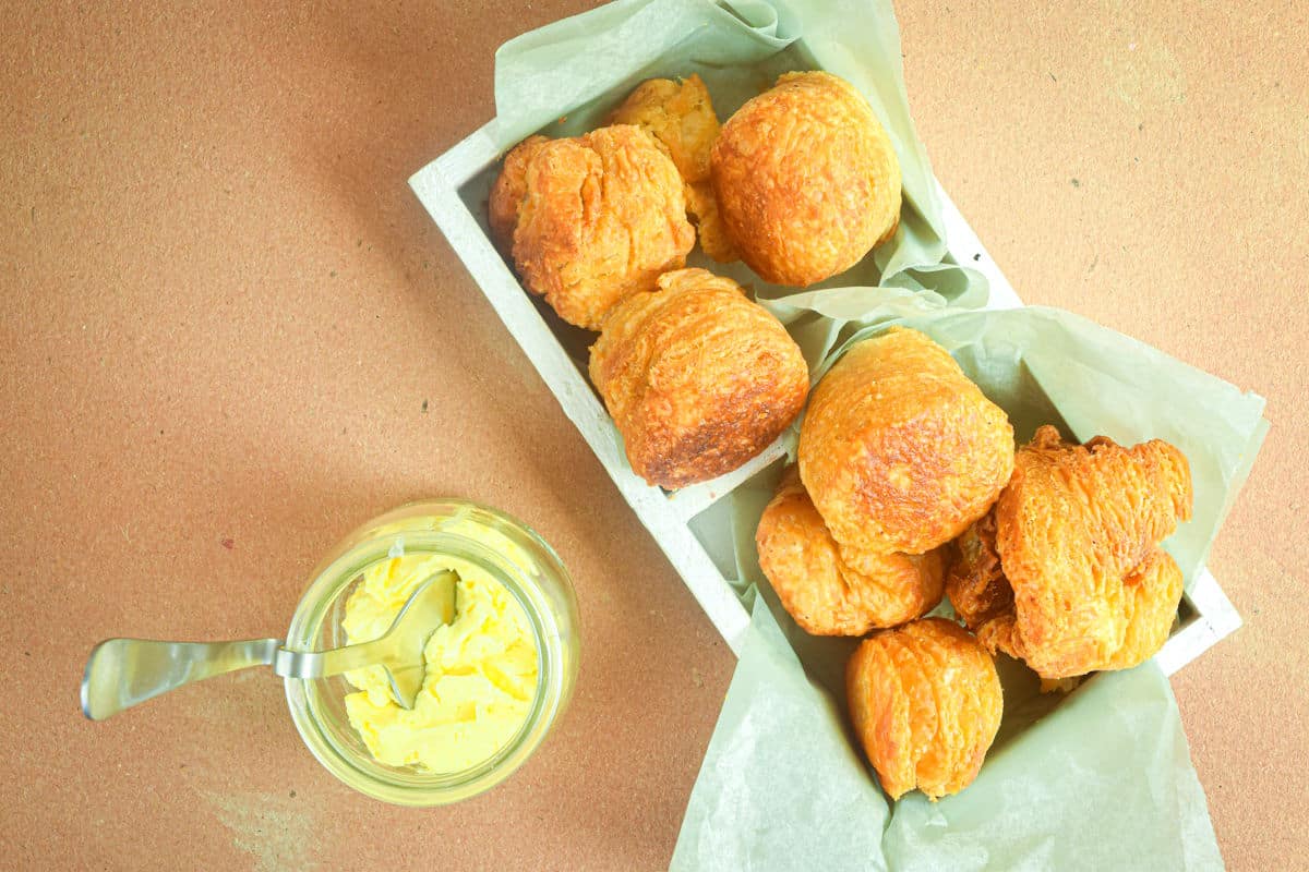 Golden biscuits in white wooden serving tray with honey butter on the side.
