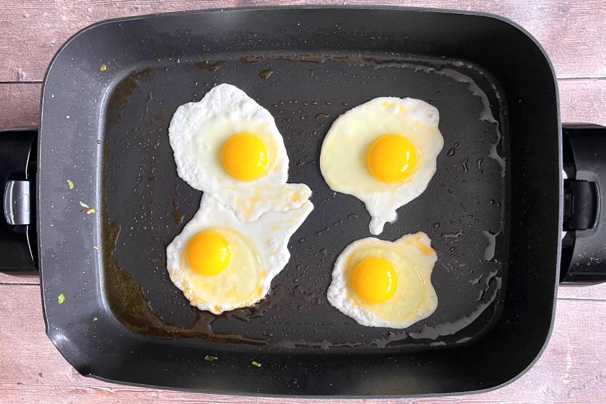 Sunny side up eggs frying in electric skillet.