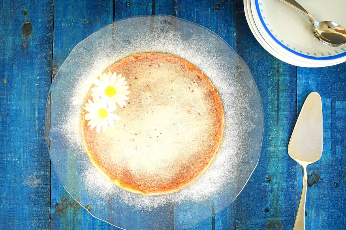 Electric skillet yogurt cake on clear glass plate with cake server.