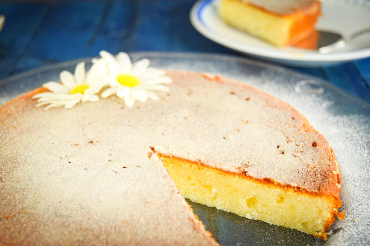 Electric skillet yogurt cake on clear glass plate with slice removed.