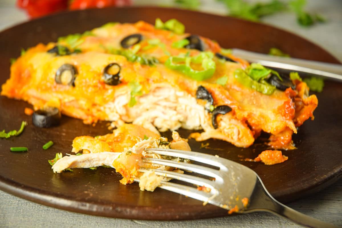 Electric skillet chicken enchiladas on brown plate with fork.