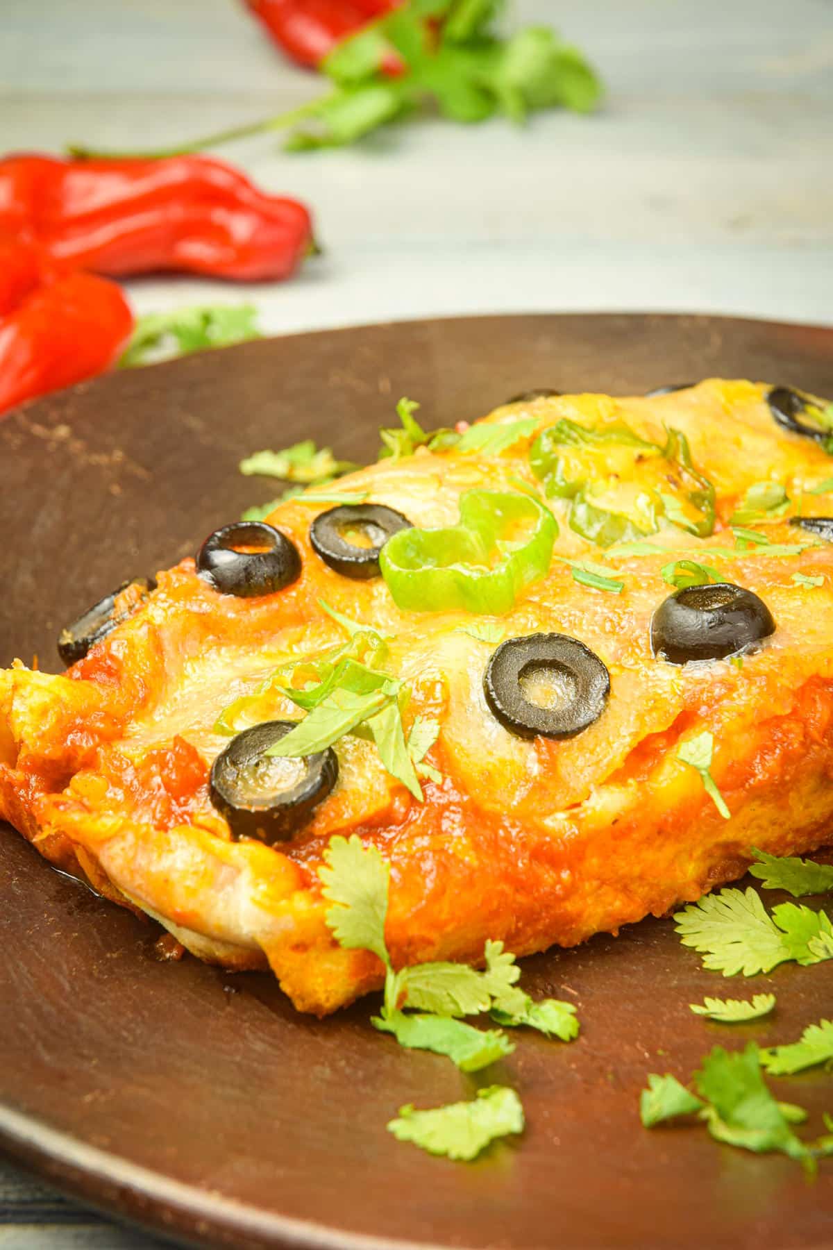 Electric skillet enchiladas on brown plate with fresh cilantro.