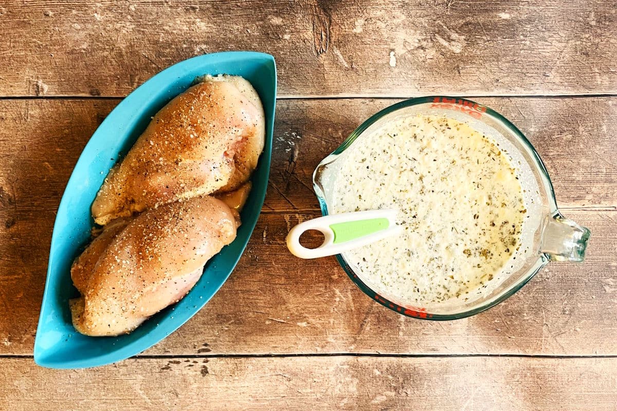 Seasoned chicken breast and creamy Tuscan sauce on wooden background.