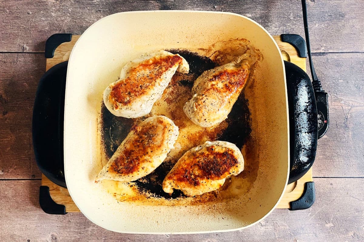 Seared chicken breasts in ceramic electric skillet.