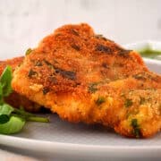 Electric skillet fried fish on white plate with fresh basil.