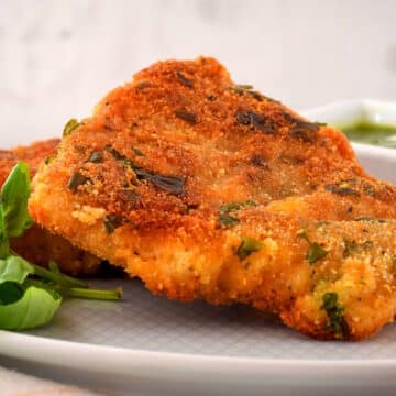 Electric skillet fried fish on white plate with fresh basil.