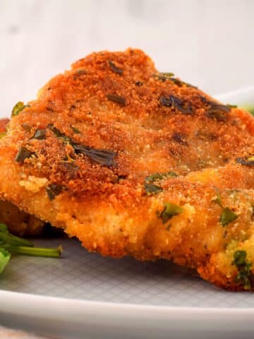 Electric skillet fried fish on white plate with fresh basil.