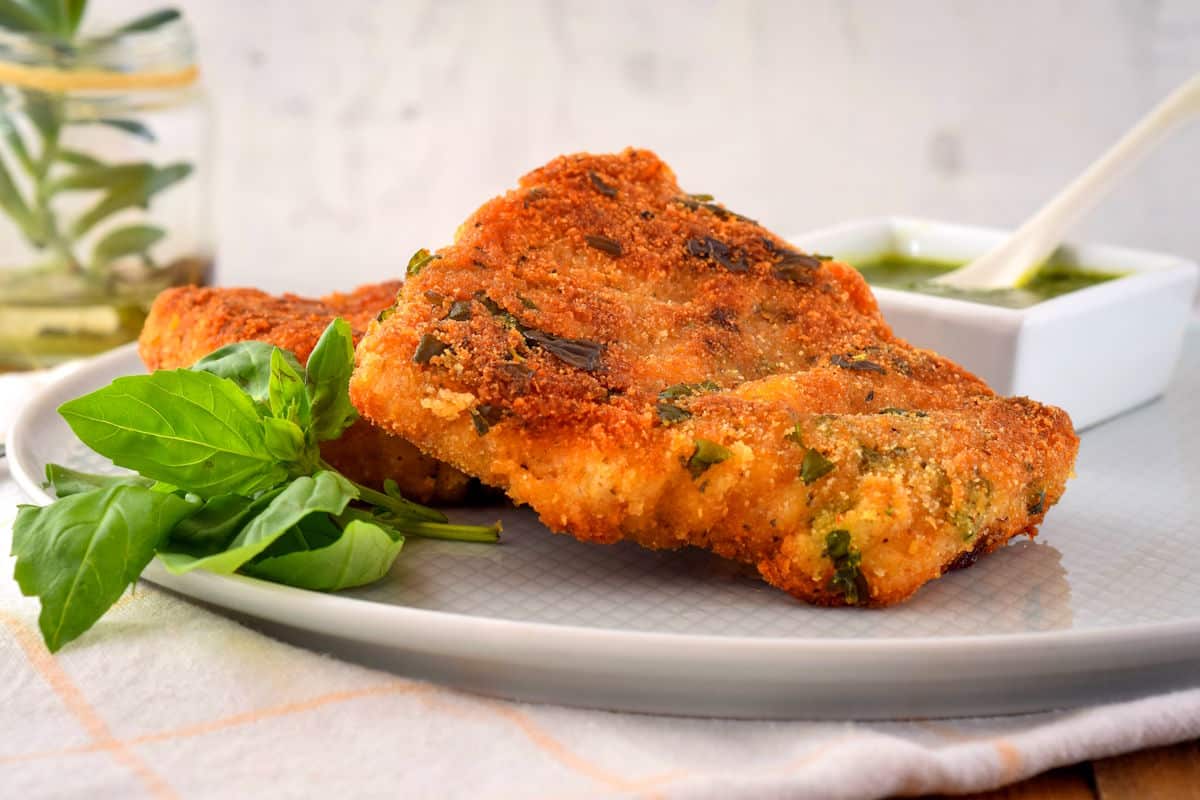 Electric skillet fried fish on white plate with fresh basil.