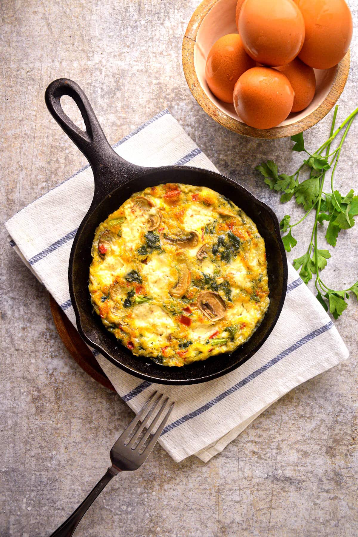 Electric skillet frittata in pan with fresh eggs on the side.