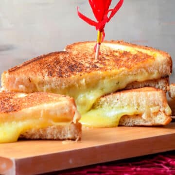 Electric skillet grilled cheese sandwiches stacked on serving board.