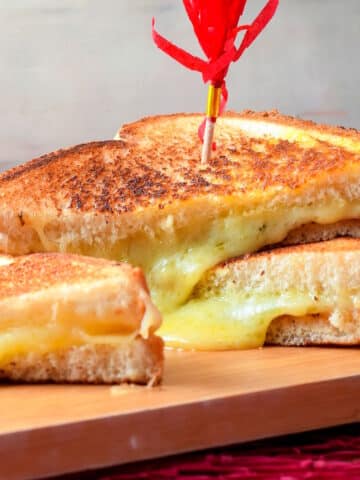 Electric skillet grilled cheese sandwiches stacked on serving board.