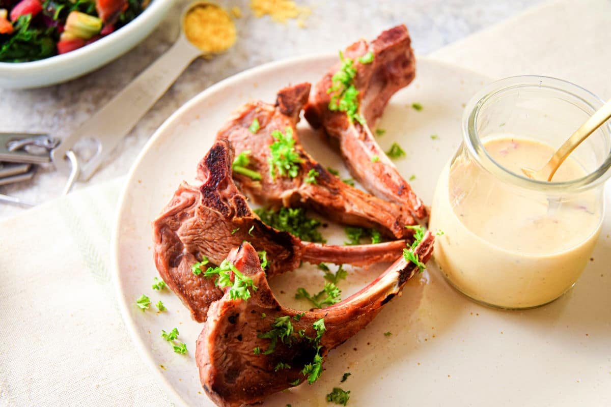 Lamb chops on plate with jar of sauce.