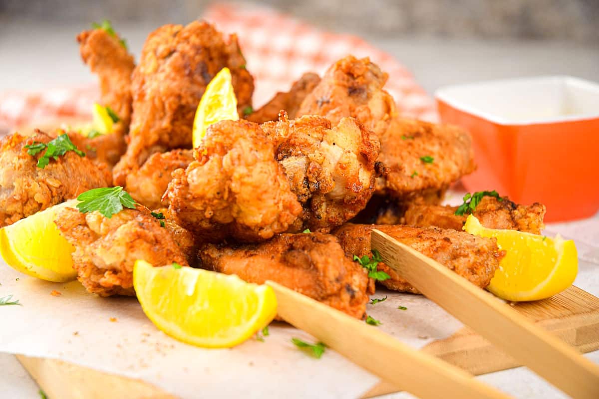Lemon pepper chicken wings with lemon wedges on serving board.