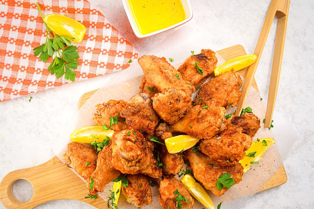 Lemon pepper chicken wings with lemon wedges on serving board, lemon butter on the side.