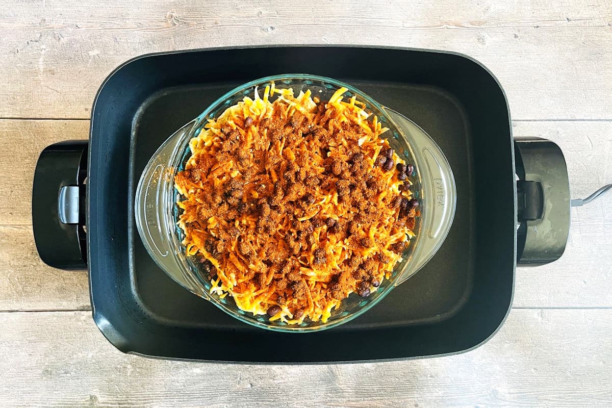 Nachos in pie dish placed in electric skillet.
