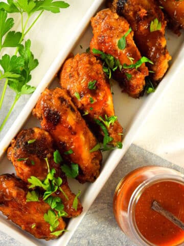 BBQ buffalo wings in dish with sauce on the side.
