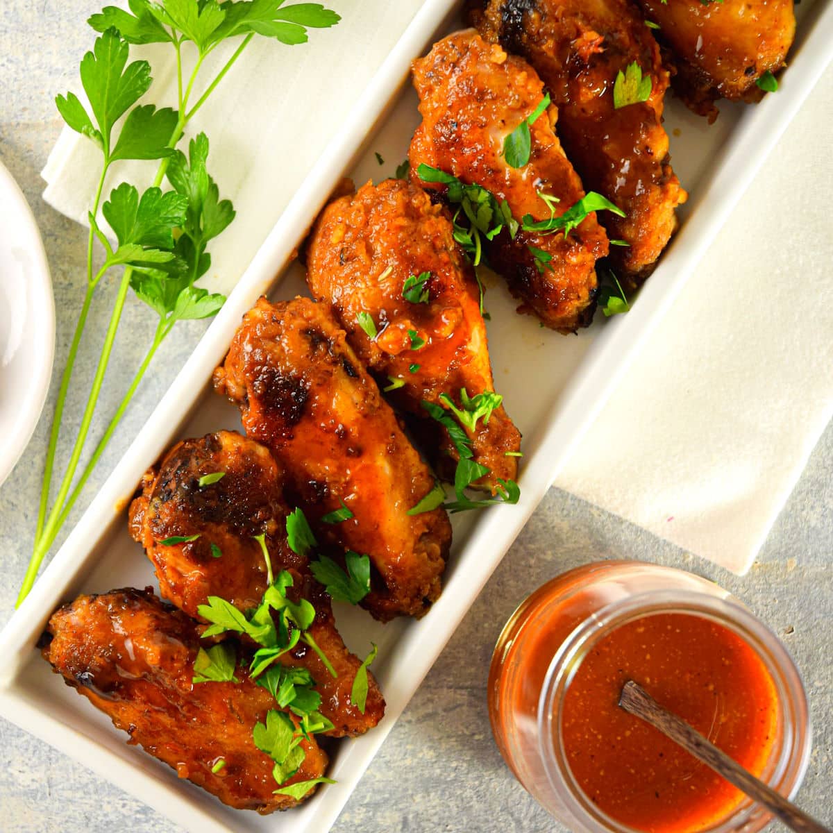 BBQ buffalo wings in dish with sauce on the side.