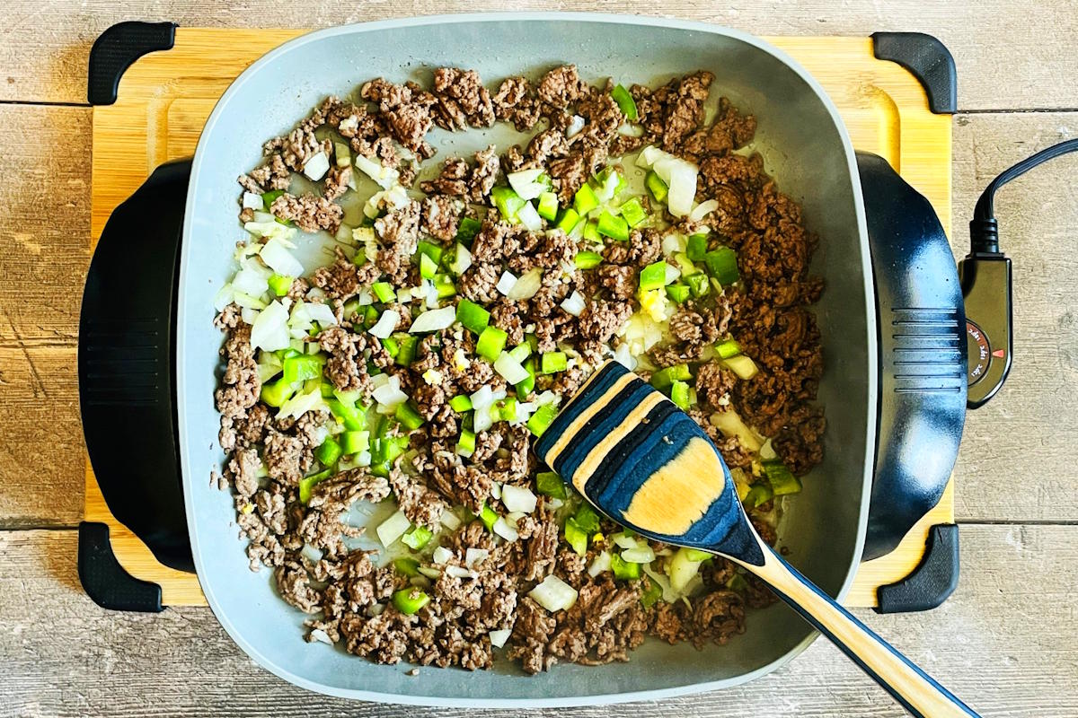 Ground beef and vegetable mixture cooking in electric skillet.