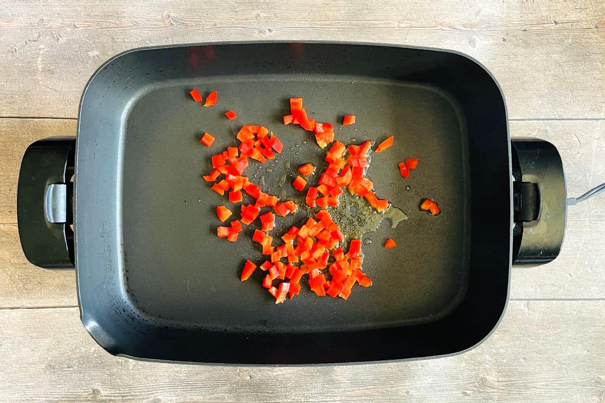 Diced red bell peppers in electric frying pan.