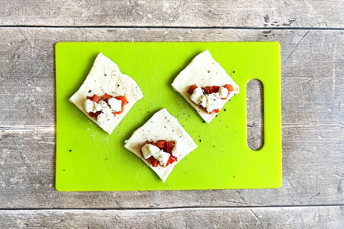 Puff pastry triangles stuffed with cheese and red peppers on board.