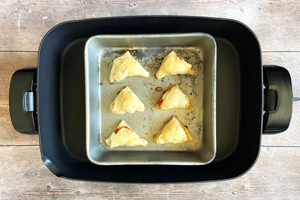 Puff pastry triangles in baking pan in electric skillet.