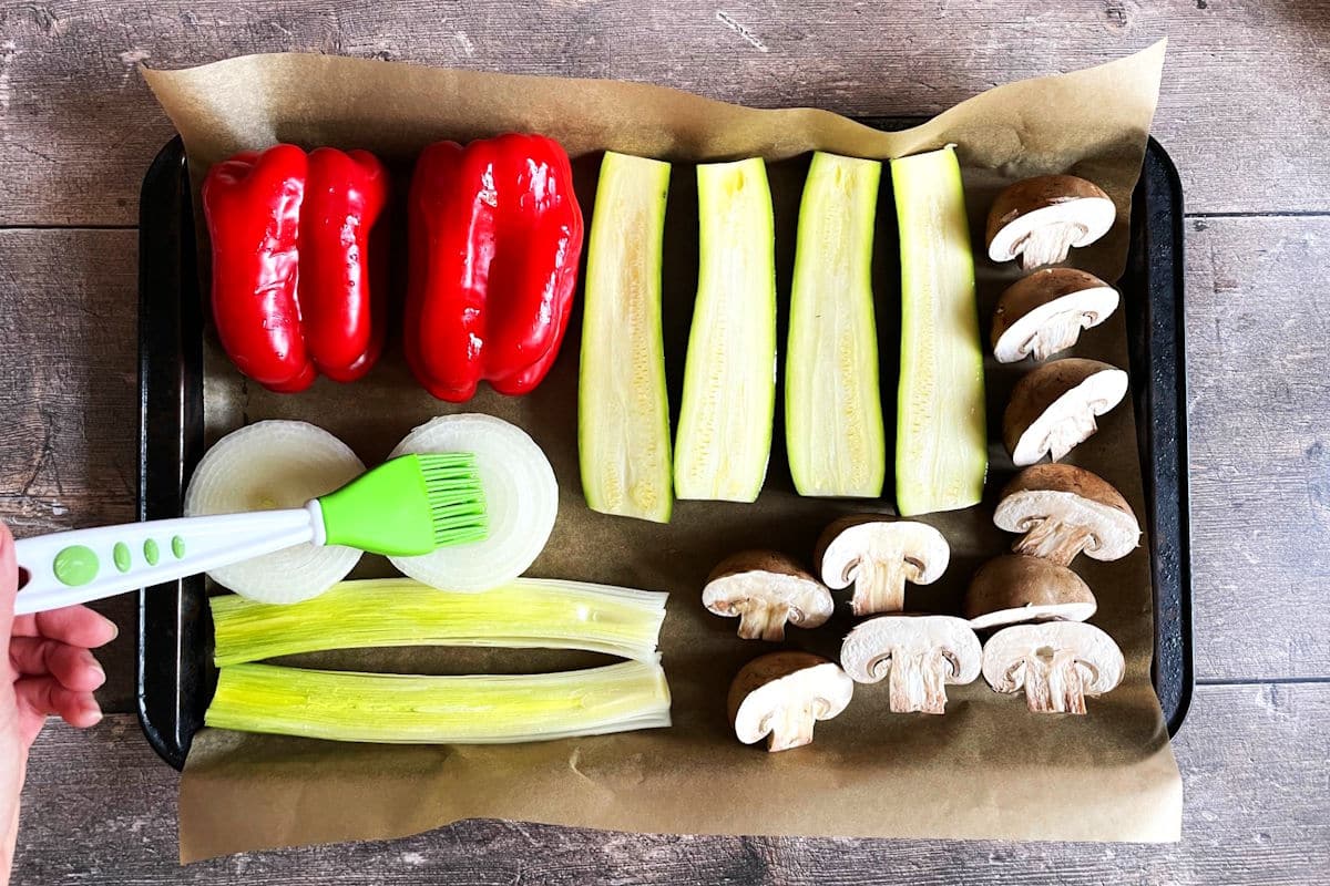 Vegetables on sheet pan getting brushed with oil.