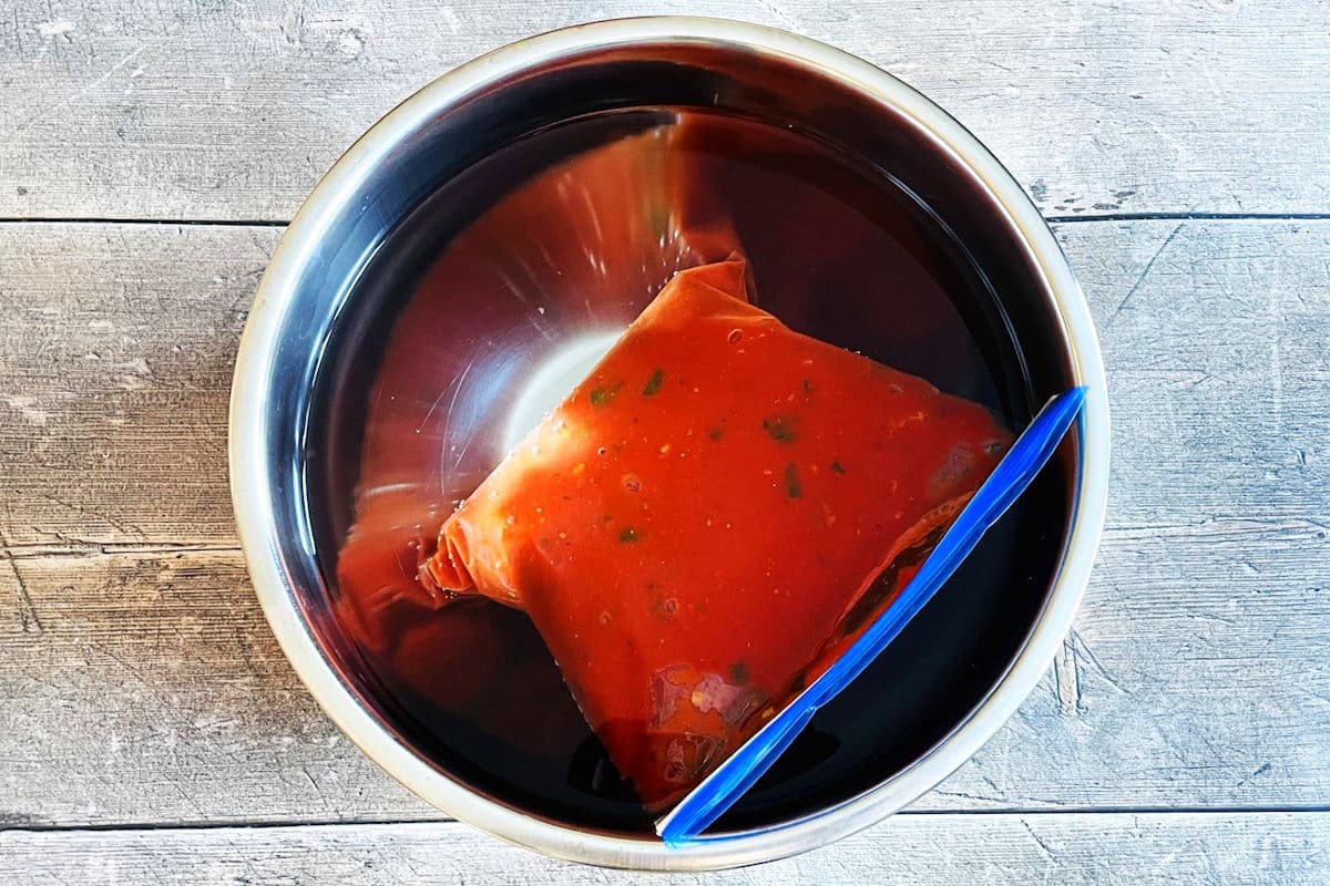 Tomato sauce package in bowl of cool water.