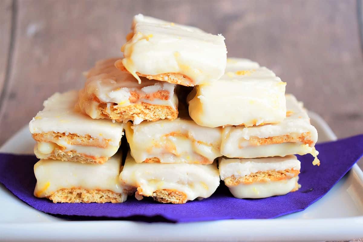 Graham wafer lemon bars stacked on purple napkin lined dish.
