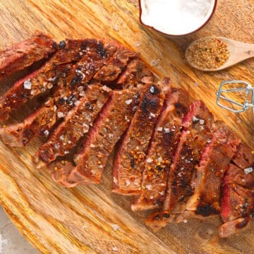 Grilled bison ribeye steak sliced on cutting board with spices on the side.