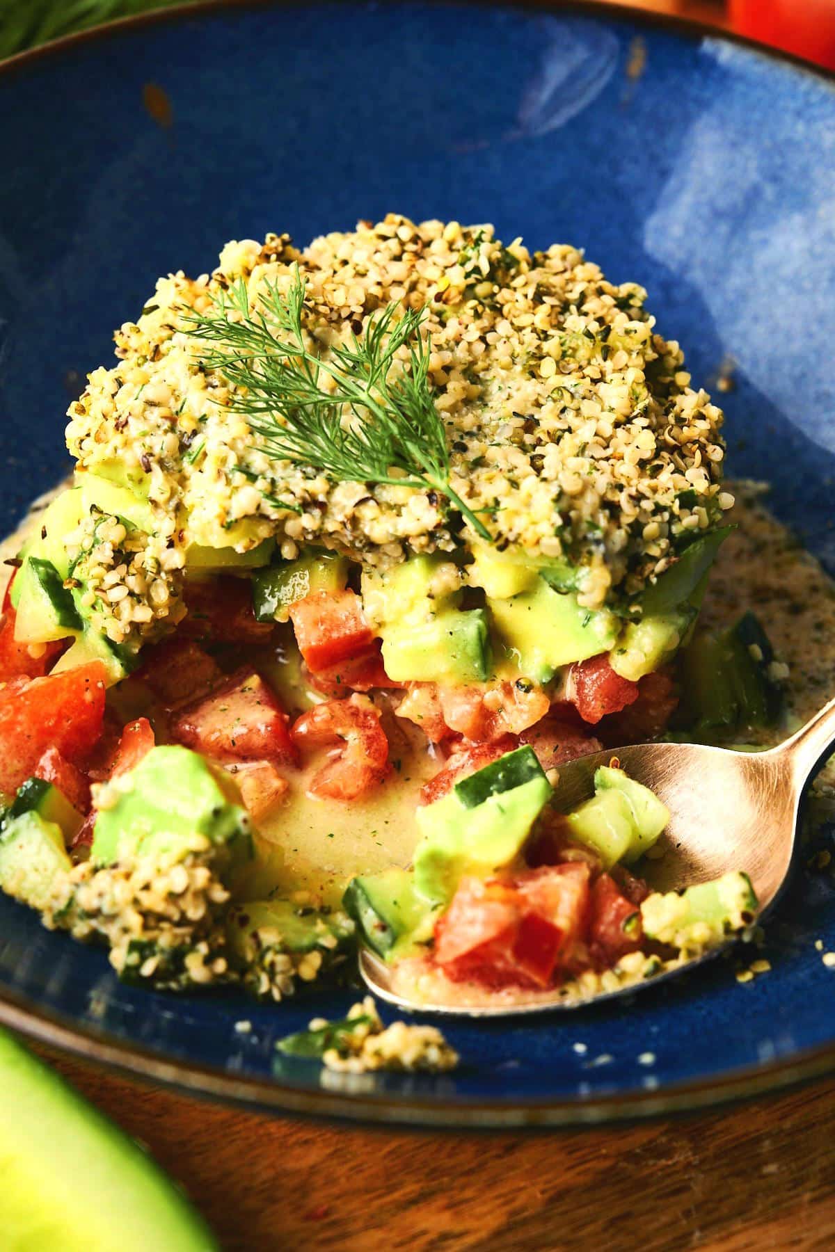 Hemp salad stacked on blue plate with a spoon.