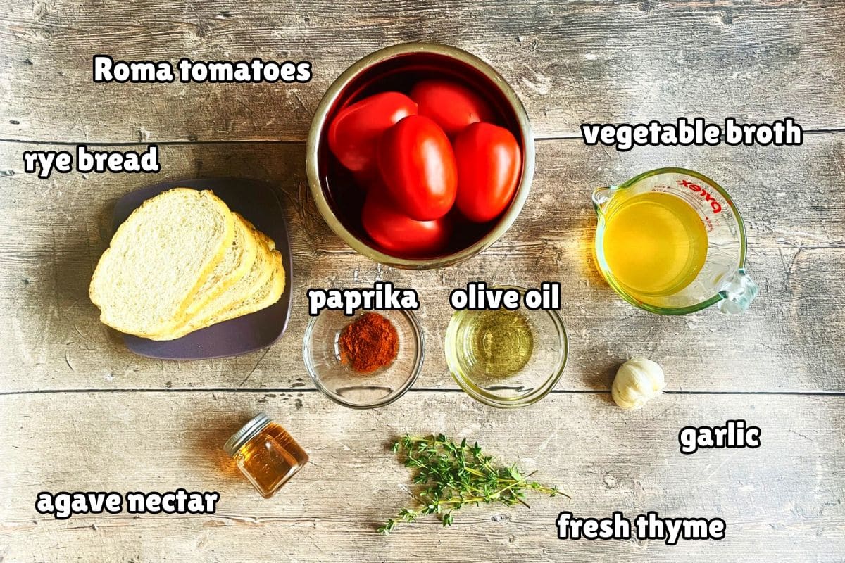 Roasted garlic tomato soup ingredients labeled on wooden background.