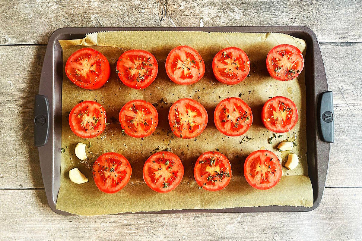 Sliced tomatoes and garlic on parchment-lined sheet pan.