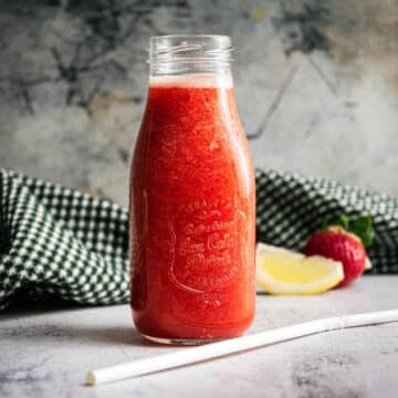 Strawberry juice in a glass jar with a white straw on the side.