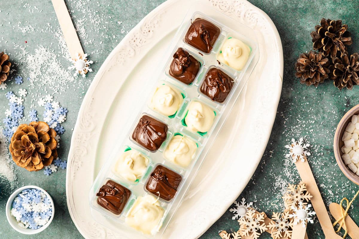 White and milk chocolate poured into ice cube tray on white serving dish.