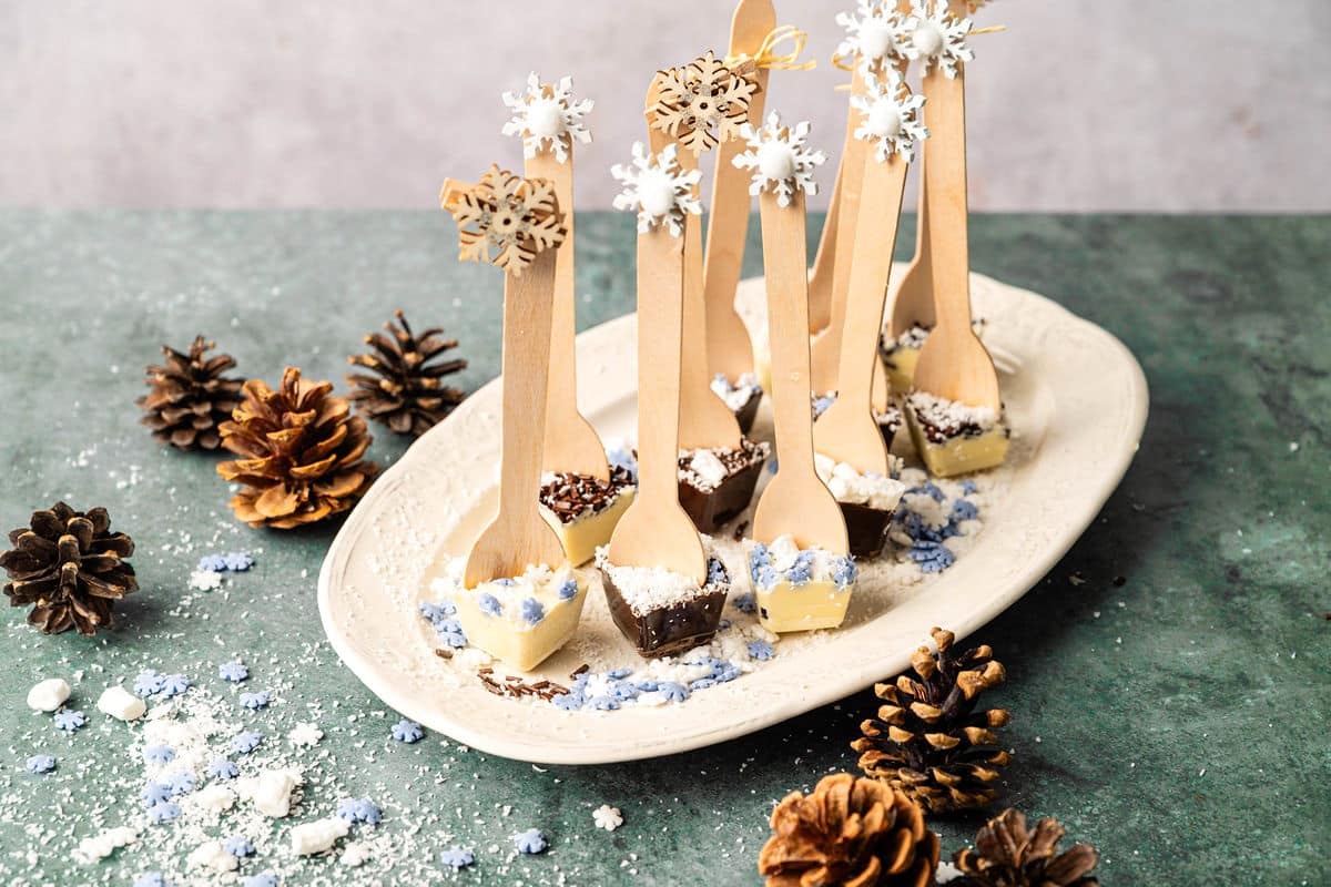 Hot chocolate spoons on white serving tray with winter decorations.