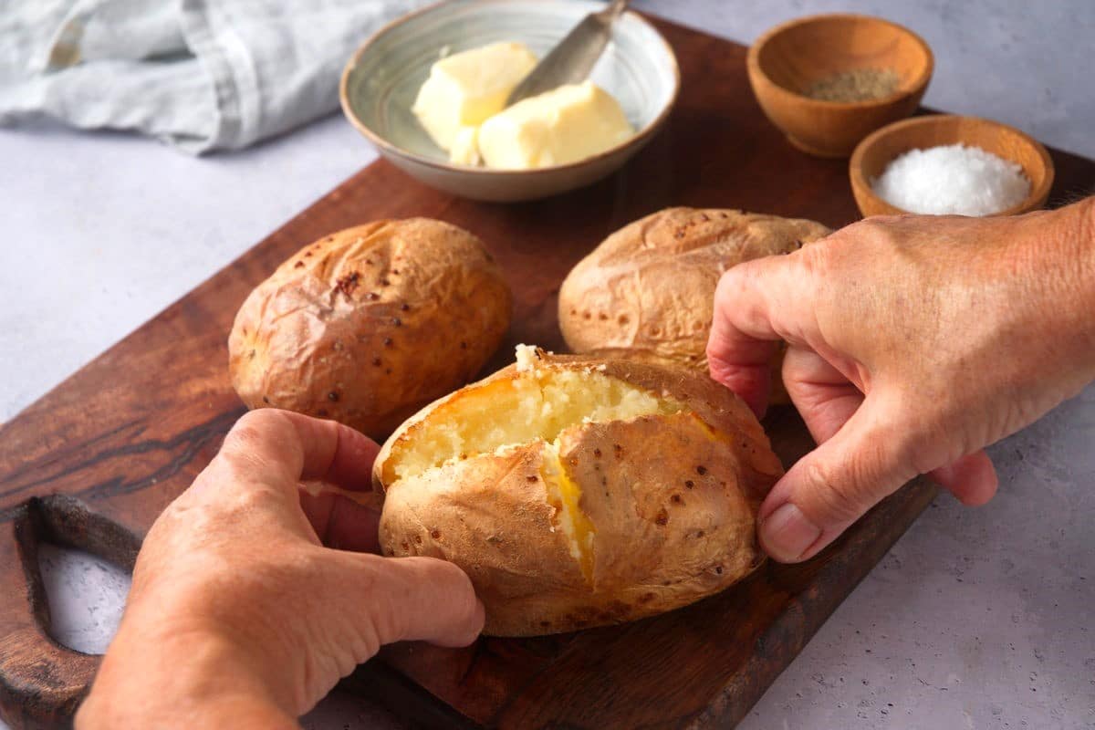 Hands holding baked potato on cutting board.