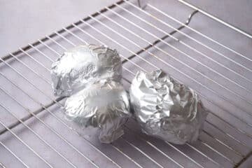 Baked potatoes in foil on oven rack.