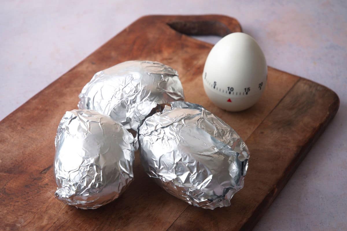 Baked potatoes in foil on cutting board with timer.
