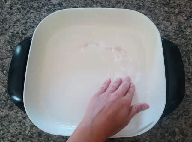 Electric skillet with baking soda paste and a hand.