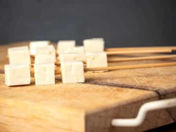 Skewered tofu cubes on cutting board.