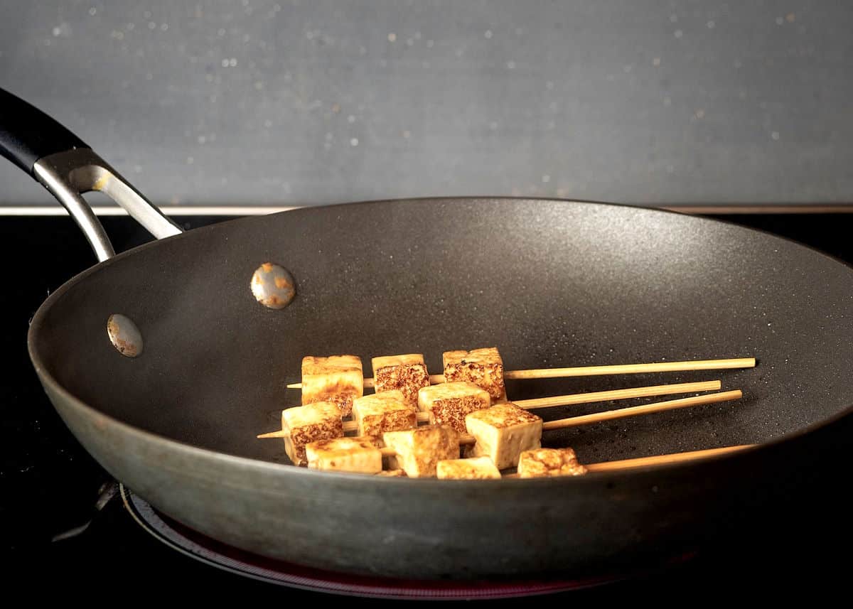 Skewered, cubed tofu in frying pan.