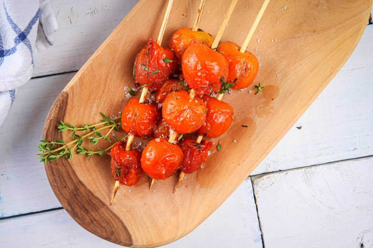 Grilled cherry tomato skewers with fresh herbs on serving tray.