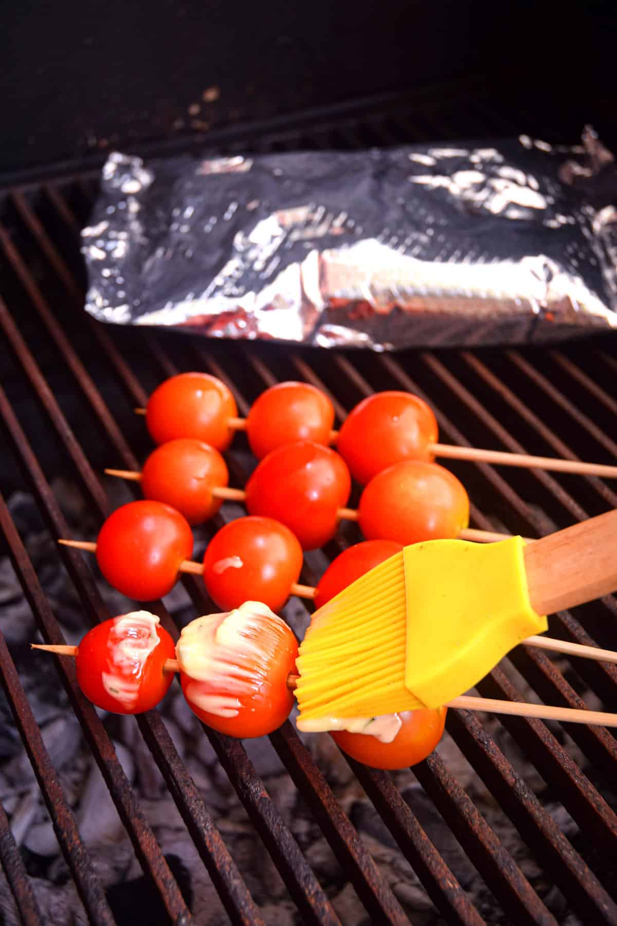 Cherry tomato skewers on grill with silicone brush.