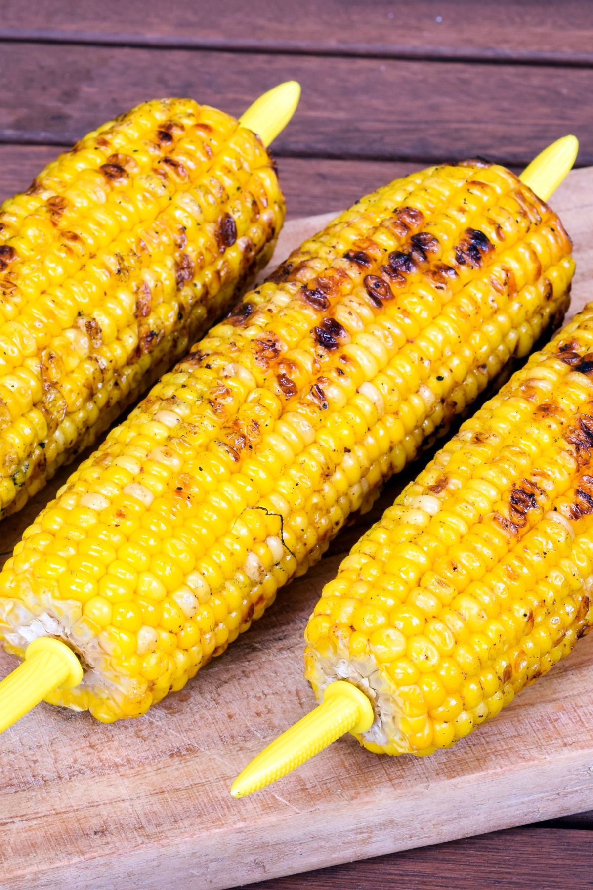 Grilled corn on the cob with corn forks on wooden board.