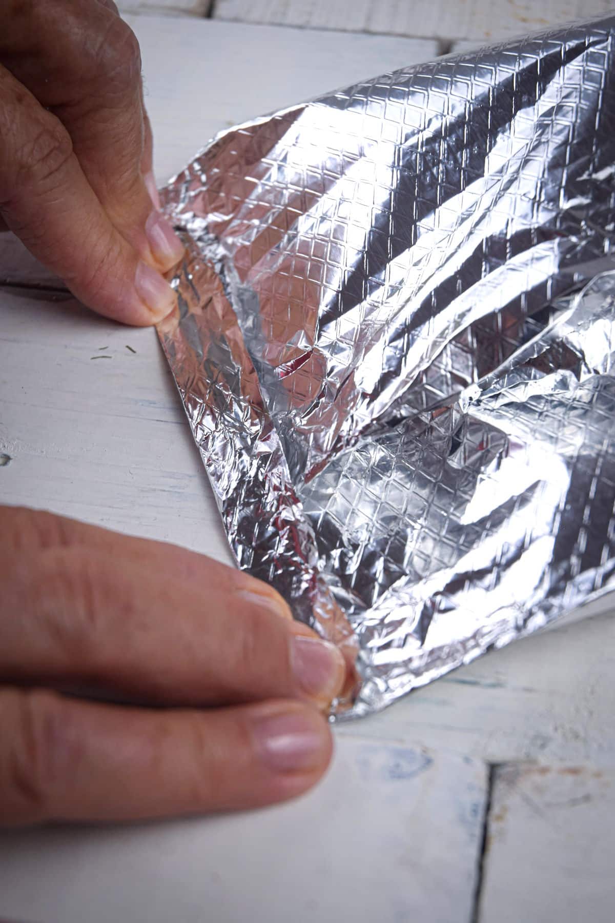 Foil pack of tomatoes getting closed by woman's hands.