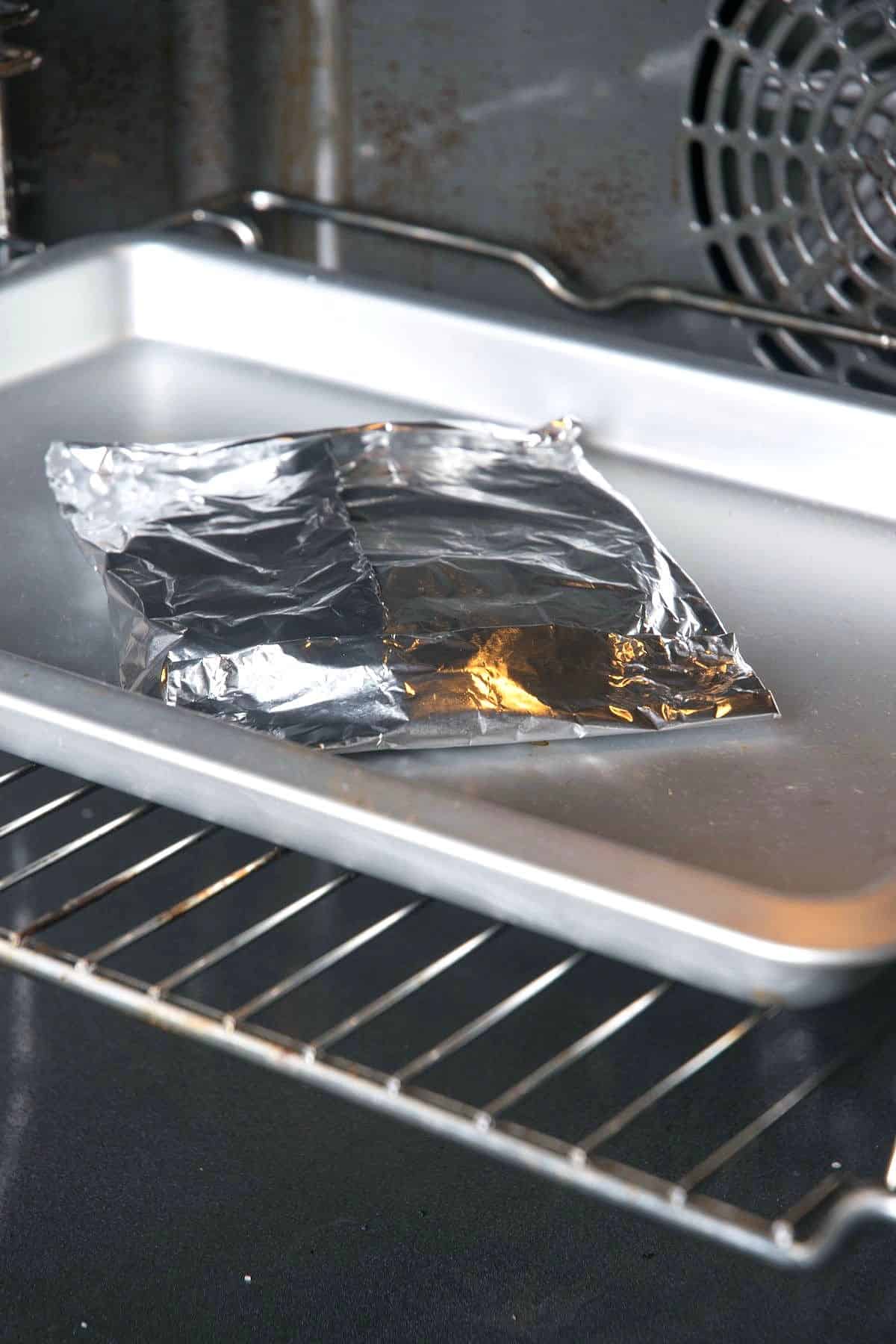 Foil pack of corn tortillas on baking sheet in oven.